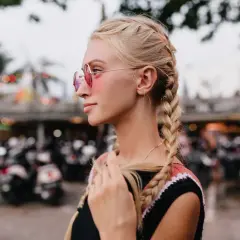 Blondynka w okularach przeciwsłonecznych z dwoma warkoczami na tle skuterów.