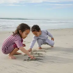 Dwoje dzieci oddaje się beztroskim zabawom na plaży, rysując palcami wzory na mokrym piasku.