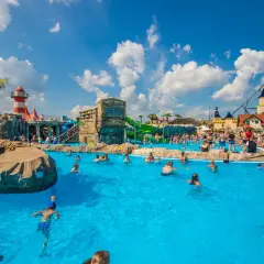 Energylandia strefa wodna tętni życiem. Ludzie kąpią się w basenie, bawią na zjeżdżalniach, a w tle widać rollercoaster.