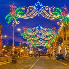 Malta w grudniu rozświetlona świątecznymi iluminacjami. Ulica ozdobiona girlandami z gwiazd i kwiatów, w tle kościół i sklepy.