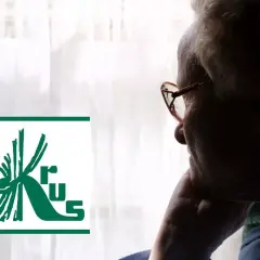 Starsza osoba w okularach patrzy przez okno, obok logo KRUS. Myśli o wcześniejsza emerytura krus.