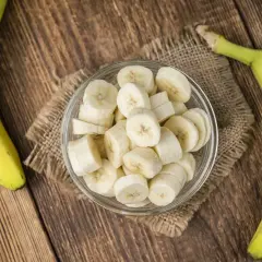 Dwa banany, jeden w całości, drugi pokrojony w plasterki w szklanej miseczce. Zastanawiasz się, ile węglowodanów ma banan?
