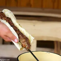 Ręka trzyma lula kebab zawinięty w placek. Mięso jest soczyste i rumiane, gotowe do jedzenia.