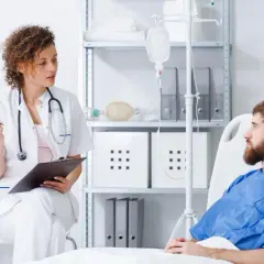 Lekarka rozmawia z pacjentem o jego leczeniu, w tym o możliwościach immunoterapii. W tle kroplówka i sprzęt medyczny.