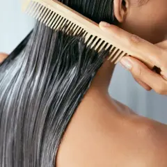 Persona peina su mascarilla en pelo seco antes de lavar, preparándolo para un tratamiento intensivo.