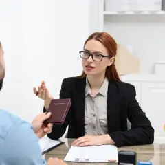 Rozmowa o średnich zarobkach w Niemczech. Konsultantka przekazuje paszport klientowi, obok flaga Niemiec.