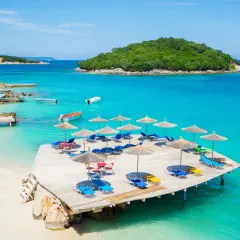 Rajskie albania plaże z turkusową wodą, drewnianym molo i leżakami pod parasolami.