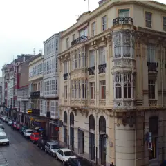 Edificios con balcones acristalados y una torre ornamental en una calle de Ferrol. Merece la pena visitar Ferrol por su arquitectura única.