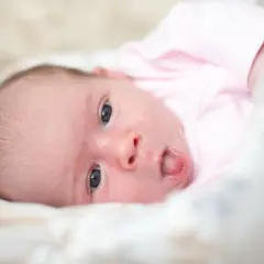 Neonato con lingua bianca, vestito di rosa, guarda incuriosito.