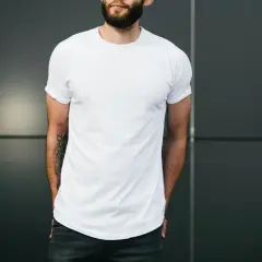 Mann mit Bart trägt weißes T-Shirt und Jeans, Hände in den Taschen.