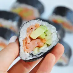 Ręka trzyma sushi z łososiem wędzonym na gorąco, awokado i ogórkiem.