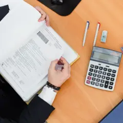 Persona in giacca e cravatta esamina documenti per i fine lavori CILA, con calcolatrice e penne a portata di mano.