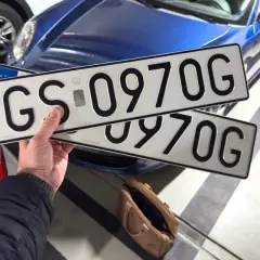 Ręka trzyma tablice rejestracyjne GS 0970G, gotowe do rejestracji samochodu online.