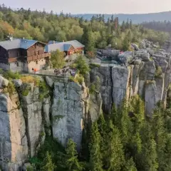 Schronisko na skalnej półce, otoczone lasem, z widokiem na wysokie góry.