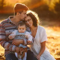 Piękne zdjecia rodzinne w złotym świetle zachodzącego słońca. Tata obejmuje córeczkę, mama wtula się w tatę.