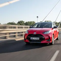 Czerwony Toyota Yaris Hybrid pędzi po moście w słoneczny dzień.
