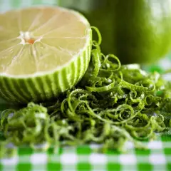 Połówka limonki i jej skórka na zielono-białej kratce. Czy limonka jest zdrowa? Tak, to cytrus pełen witamin!