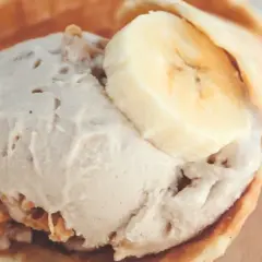Delicioso helado de crema de cacahuete en un cono de gofre, coronado con rodajas de plátano.