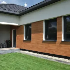 Nowoczesny dom z drewnopodobną elewacją, która jest jednym z najmodniejszych kolorów elewacji. Ciemne okna i białe detale tworzą elegancką całość.