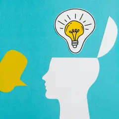 Psychologia obrazki: biała głowa z otwartą czaszką, w której świeci żarówka pomysłu, obok żółty dymek.