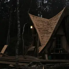 En magisk koja i skogen med ett spetsigt tak av träspån. En ensam stol står på altanen, redo för en stunds avkoppling.