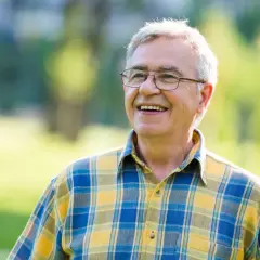 Uśmiechnięty starszy mężczyzna w okularach i koszuli w kratę na tle zieleni.