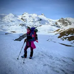 Una mujer con mochila y bastones disfruta de excursiones nieve en un paisaje montañoso cubierto de blanco.