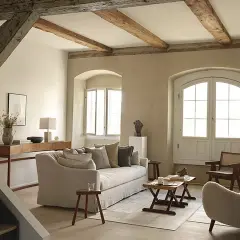 Soggiorno accogliente con pareti color sabbia tortora, travi a vista e arredi in lino e legno.