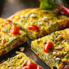 Tortilla de acelgas con tomates cherry y piñones, cortada en porciones sobre una tabla de madera.