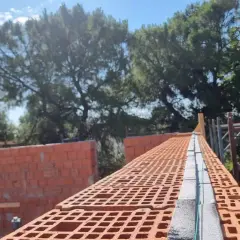 Costruzione di una muratura portante in laterizio, con mattoni forati rossi e blocchi in cemento.
