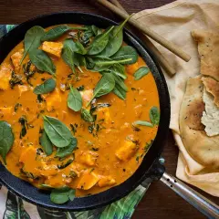 En krämig palak paneer halloumi i en gjutjärnspanna, toppad med färsk spenat. Bredvid ligger naanbröd.