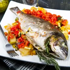 Dorada a la gallega, entera y horneada, servida sobre una cama de verduras picadas, con romero fresco.