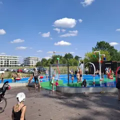 Dzieci bawią się na wodnym placu zabaw przy zalewie Borki. Woda tryska z kolorowych elementów, tworząc radosną atmosferę.