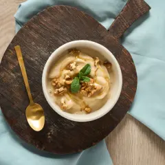 En skål med krämig nice cream, toppad med valnötter, mynta och honung. En gyllene sked ligger bredvid.