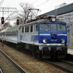 Niebieski pociąg TLK EU07-067 z wagonami PKP Intercity stoi na torach obok peronu.