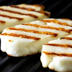 Trzy kawałki halloumi z grilla, z charakterystycznymi brązowymi paskami, leżą na czarnej, żebrowanej powierzchni.