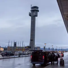 Wieża kontrolna lotniska Oslo Gardermoen, samochody i ludzie przy terminalu.