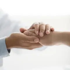 Dłoń lekarza w białym kitlu pociesza dłoń pacjenta. Symbol niepełnosprawności 02-p dofinansowanie.