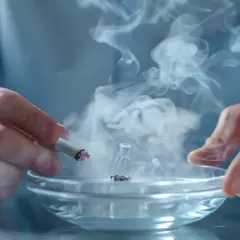 Dym z papierosa unosi się nad popielniczką. Nikotyna wciąga w swój nałóg.