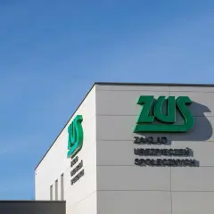 Budynek ZUS z zielonym logo i napisem "Zakład Ubezpieczeń Społecznych" na tle błękitnego nieba.