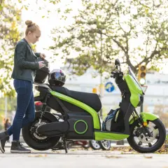 Mujer con casco y móvil junto a ciclomotor eléctrico verde. ¿Cuál será su velocidad máxima?