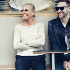 Joakim Berg familj: en kvinna och en man sitter på en bänk utanför ett café, båda ler och bär solglasögon.