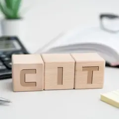 Drewniane klocki z napisem CIT, kalkulator, okulary i książka. Kto płaci podatek CIT?
