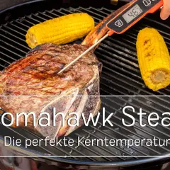 Ein saftiges Tomahawk Steak wird auf dem Grill mit Maiskolben gegrillt. Ein Fleischthermometer misst die Kerntemperatur für das perfekte Ergebnis.