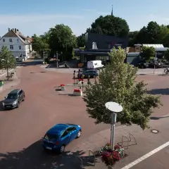Ein sonniger Tag im **shared space Bohmte**. Autos fahren durch den Kreisverkehr, ein Radfahrer genießt die Fahrt.