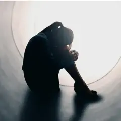 Silhouette di una persona rannicchiata in un tunnel, simbolo di solitudine e mancanza di affetto.