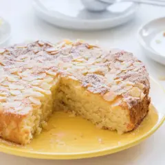 Saftiger Kuchen ohne Mehl, bestreut mit Mandelblättchen und Puderzucker. Dazu Zitronenspalten und eine ganze Zitrone.
