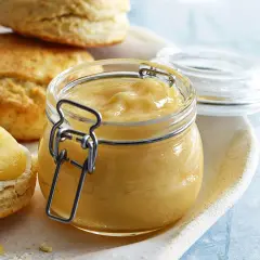 En burk med hemgjord lemon curd står bredvid scones. Perfekt för ditt lemon curd recept!