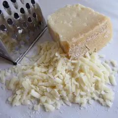 Un pezzo di formaggio a pasta cotta accanto a una grattugia, con formaggio grattugiato sparso.