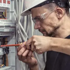 Technik elektryk w okularach ochronnych i kasku precyzyjnie dokręca śrubę w skrzynce rozdzielczej.
